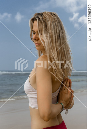 Back view of fit faceless female in activewear standing on seashore and practicing meditation while doing yoga on beach 122696369