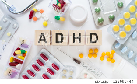 Abbreviation on ADHD (Attention Deficit Hyperactivity Disorder) cubes on wooden blocks on the table. Medical concept with pills, vitamins, stethoscope and syringe in the background. 122696444