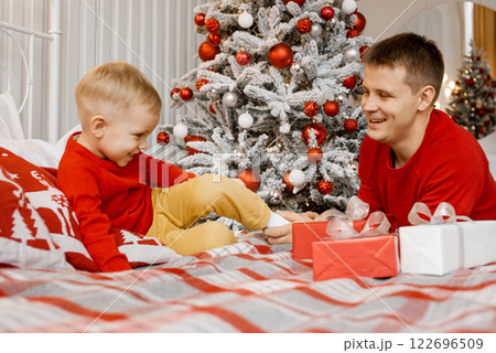 Young cheerful dad hold his son's leg and tickle it while his laughing little son trying to escape over Christmas tree background 122696509