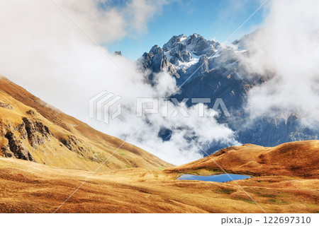 Autumn landscape and snow mountains in beautiful cumulus clouds. Main Caucasian Ridge. Type Mount Ushba Mheyer, Georgia Autumn landscape and snow mountains in beautiful cumulus clouds. Main Caucasian Ridge. Type Mount Ushba Mheyer, Georgia 122697310