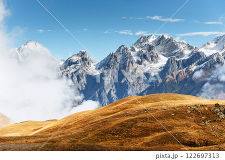 Autumn landscape and snow mountains in beautiful cumulus clouds. Main Caucasian Ridge. Type Mount Ushba Mheyer, Georgia 122697313