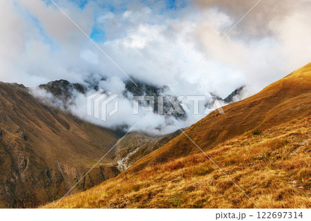 Autumn landscape and snow mountains in beautiful cumulus clouds. Main Caucasian Ridge. Type Mount Ushba Mheyer, Georgia 122697314