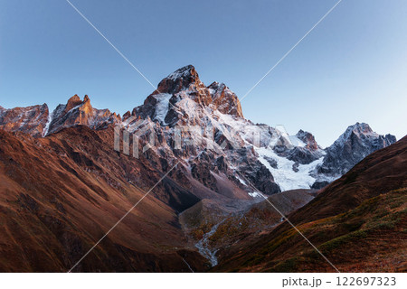 Autumn landscape and snow mountains in beautiful cumulus clouds. Main Caucasian Ridge. Type Mount Ushba Mheyer, Georgia 122697323