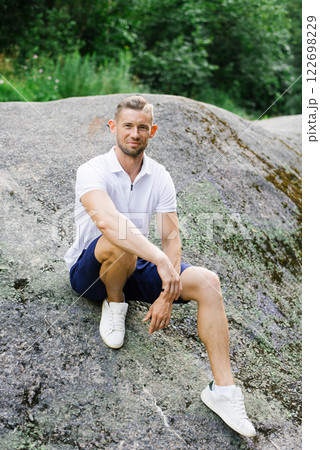 Relaxed Man Sitting Comfortably On Large Rock Outdoors Relaxed Man Sitting Comfortably On Large Rock Outdoors 122698229
