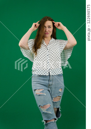 Tanned modern girl with curly hair and red lipstick in stylish wide long sleeve polka dot shirt and light jeans posing with closed eyes on balcony.. 122698575
