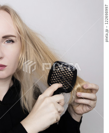 Blonde woman unhappy with her hair condition and trying to brush it. Bad hairstyle, tangled curly hair without using conditioner. 122698997