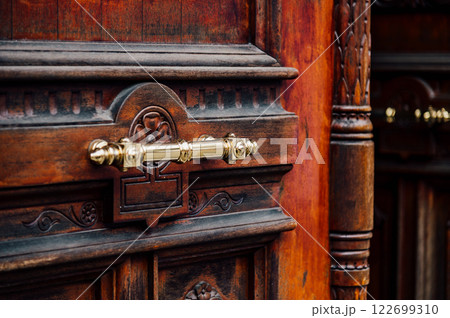 Intricate detail of an antique wooden door with ornate carvings and a brass handle. Rich textures and warm tones create a sense of history and elegance. 122699310