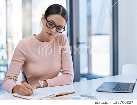 Planning, thinking and strategy with business woman writing notes while working on a laptop in a corporate office. Professional assistant plan schedule and meetings, using journal to write reminder 122700824
