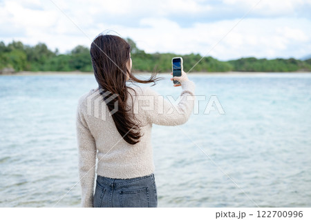 海を眺めながら写真を撮る女性 122700996