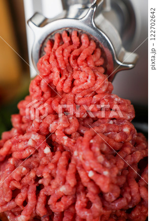 The concept of healthy and proper nutrition, cooking. A close-up view from above of red ground beef with streaks of fat, which comes out of the metal grinder in waves and takes up most of the photo The concept of healthy and proper nutrition, cooking. A close-up view from above of red ground beef with streaks of fat, which comes out of the metal grinder in waves and takes up most of the photo 122702642