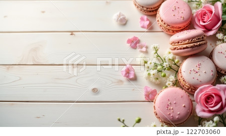 Assorted pastel macarons with pink roses and petals on a rustic white wooden table. Flat lay composition with copy space 122703060