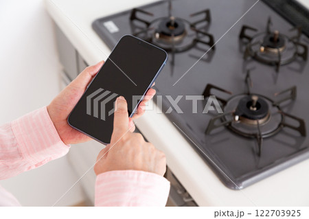 賃貸マンションのガスコンロの前でスマホを持つ中年女性の手元 122703925