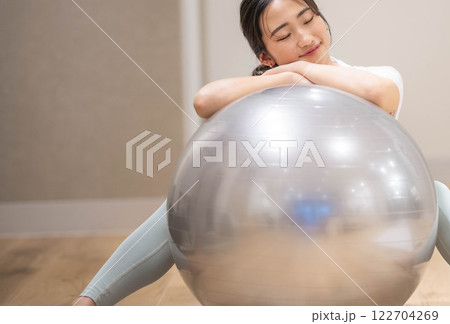 室内のジムでバランスボールを使用しエクササイズする若い女性 122704269