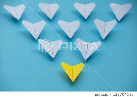 Straight view of yellow paper airplane origami leading other white airplanes on blue background with customizable space for text. Business and Leadership skills concept 122704516
