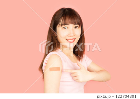 Asian woman showing vaccinated arm with medical adhesive bandage strip after vaccine injection over pink background. Concept of HPV vaccine, world immunization day and vaccinations in pregnancy. Asian woman showing vaccinated arm with medical adhesive bandage strip after vaccine injection over pink background. Concept of HPV vaccine, world immunization day and vaccinations in pregnancy. 122704801