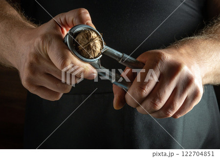 Hands skillfully use a metal nutcracker to break open a walnut, revealing the rich, textured shell and inner nut. The warm ambiance adds a touch of tradition and craftsmanship to the moment. 122704851