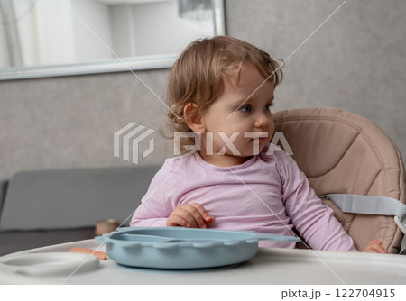 A curious toddler distracted during mealtime, observing something with focused attention. 122704915