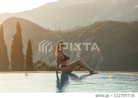 Slim woman in swimsuit walking by the edge of luxury infinity pool with jungle view Slim woman in swimsuit walking by the edge of luxury infinity pool with jungle view 122705716