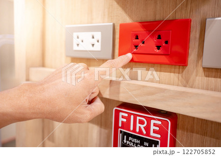 Hand pointing at red electric socket or power plug outlet on wooden wall with a fire alarm switch 122705852
