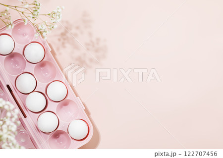 White eggs in pink container adorned with delicate floral accents on soft pastel pink background. Minimalist and elegant concept perfect for holiday Easter celebrations and spring themes. Copy space 122707456