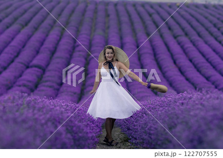 A woman in a white dress is standing in a field of purple flowers 122707555