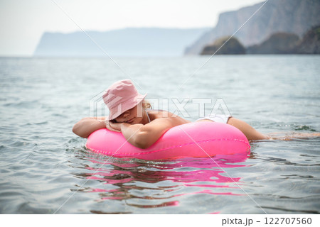 A woman is laying on a pink inflatable raft in the ocean. The scene is peaceful and relaxing, with the woman enjoying the water and the sun. A woman is laying on a pink inflatable raft in the ocean. The scene is peaceful and relaxing, with the woman enjoying the water and the sun. 122707560