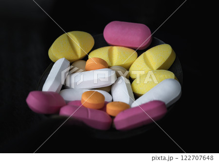 A lot of pills of different colors and shapes stacked together on black background. A lot of pills of different colors and shapes stacked together on black background. 122707648