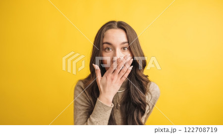 Surprised woman covering mouth on yellow background Surprised woman covering mouth on yellow background 122708719