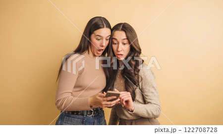 Surprised friends sharing exciting news on smartphone 122708728