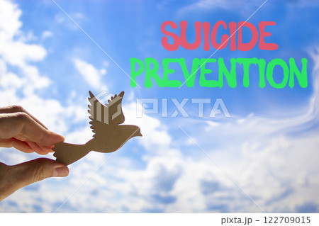 Suicide prevention symbol. Concept words Suicide prevention on beautiful blue sky. Psychologist hand, wooden bird. Beautiful blue sky background. Psychological suicide prevention concept Copy space Suicide prevention symbol. Concept words Suicide prevention on beautiful blue sky. Psychologist hand, wooden bird. Beautiful blue sky background. Psychological suicide prevention concept Copy space 122709015