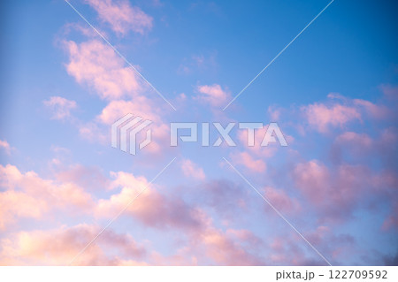 Scattered pink clouds drifting across a vibrant blue sky create a stunning sunset scene, radiating tranquility and warmth while inviting a sense of peacefulness and serenity Scattered pink clouds drifting across a vibrant blue sky create a stunning sunset scene, radiating tranquility and warmth while inviting a sense of peacefulness and serenity 122709592