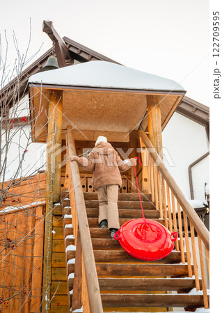 Winter scene showing a girl climbing snowy wooden stairs, pulling a red snow tube behind her, at a ski resort, ready for some fun in the snow Winter scene showing a girl climbing snowy wooden stairs, pulling a red snow tube behind her, at a ski resort, ready for some fun in the snow 122709595