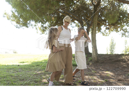 Mother engaging with children under shady tree 122709990