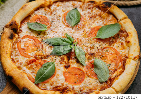 Classic Margherita pizza with fresh basil, tomatoes, and mozzarella on a wooden board 122710117