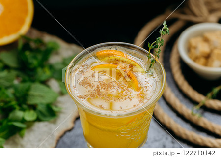 Refreshing citrus cocktail with orange slices, cinnamon and herbs in glass on dark background Refreshing citrus cocktail with orange slices, cinnamon and herbs in glass on dark background 122710142