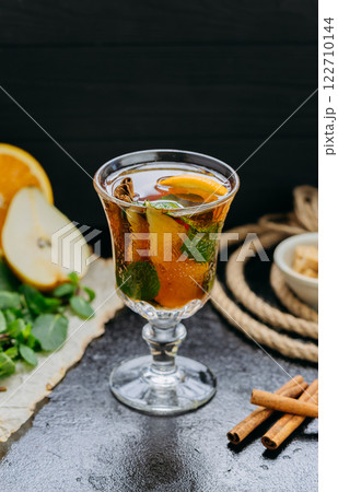 Aromatic herbal tea with citrus, cinnamon, and mint in a glass, set on a dark rustic background Aromatic herbal tea with citrus, cinnamon, and mint in a glass, set on a dark rustic background 122710144