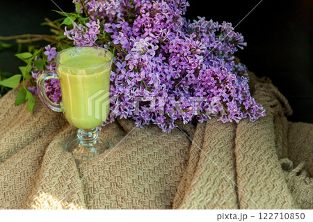 Glass mug with smoothie on the background of a bouquet of lilacs close-up 122710850