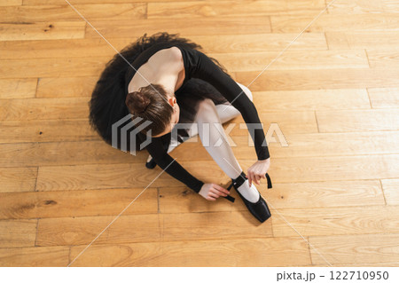 Ballerina puts on pointe shoes on leg in dance class. Classical ballet dancer woman in dance studio. Ballerina putting on tying classical pointe shoes for dance training. Ballet school concept Ballerina puts on pointe shoes on leg in dance class. Classical ballet dancer woman in dance studio. Ballerina putting on tying classical pointe shoes for dance training. Ballet school concept 122710950