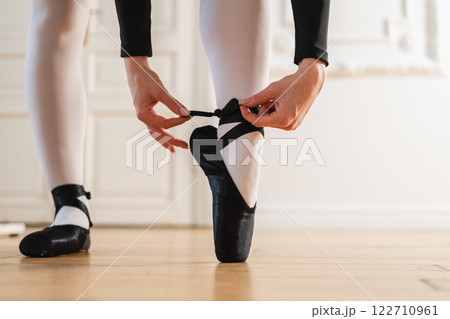 Ballerina puts on pointe shoes on leg in dance class. Classical ballet dancer woman in dance studio. Ballerina putting on tying classical pointe shoes for dance training. Ballet school concept 122710961