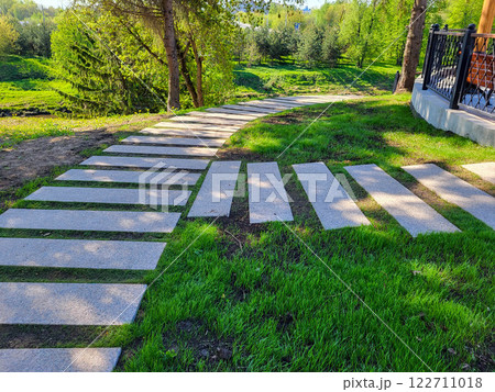 In the spring park, a path made of concrete rectangles is laid between the trees. The concept of landscaping and landscape design 122711018