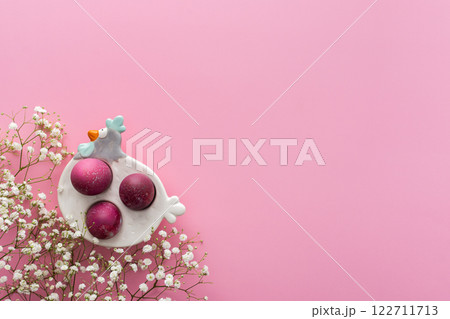 Easter eggs in a decorative hen with gypsophila flowers on a pink background 122711713