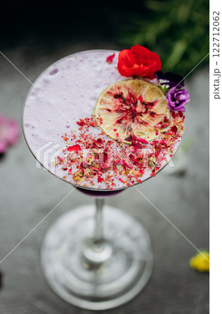Elegant purple cocktail in a martini glass, garnished with dried lime, petals, and edible flowers Elegant purple cocktail in a martini glass, garnished with dried lime, petals, and edible flowers 122712062