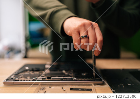 Close-up hands of unrecognizable computer master using screwdriver to repair motherboard of disassembled laptop in workshop. Concept of process electronic device repair. 122712300