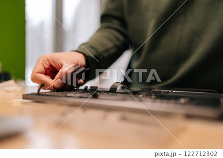 Cropped shot of technician using tweezers assembling small component on laptop motherboard, performing maintenance and troubleshooting in repair workshop. Concept of process electronic device repair. 122712302