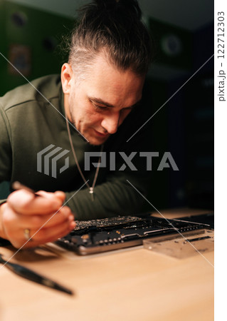 Portrait of computer technician repairing laptop motherboard, troubleshooting hardware issues in dimly lit workshop environment, demonstrating expertise in electronics maintenance. 122712303