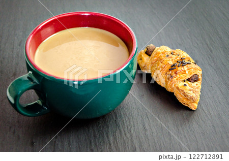 A cup of green latte and a croissant on the table with a dark background. Breakfast A cup of green latte and a croissant on the table with a dark background. Breakfast 122712891