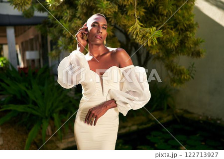 Person in elegant white dress stands at villa garden. Soft sunlight highlights the scene. Gender fluid style in bridal fashion. Modern LGBTQ theme. Trendy eco-friendly wedding venue. 122713927