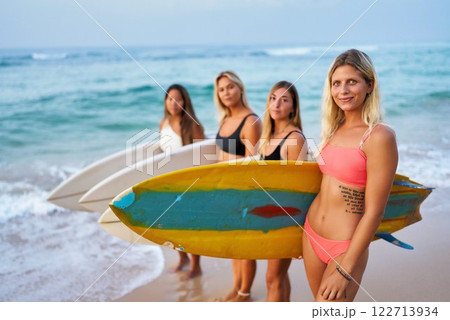 Young women with surfboards on beach. Friends enjoy summer surfing together. Female surfers in bikinis, vibrant energy, celebrate International Women Day through sport, adventure. Young women with surfboards on beach. Friends enjoy summer surfing together. Female surfers in bikinis, vibrant energy, celebrate International Women Day through sport, adventure. 122713934