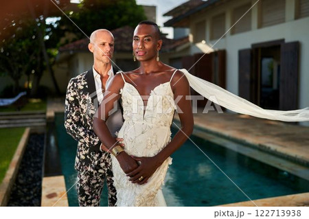 Gender-fluid couple weds at tropical villa. Bride in white dress with groom in eye-catching suit near pool. LGBTQ destination wedding. Love, diversity embraced at exotic getaway. 122713938