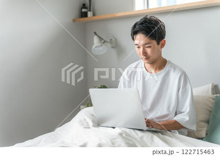 在宅勤務・テレワーク・リモートワーク・在宅ワークで朝ベッドルームでパソコンを使う男性 122715463